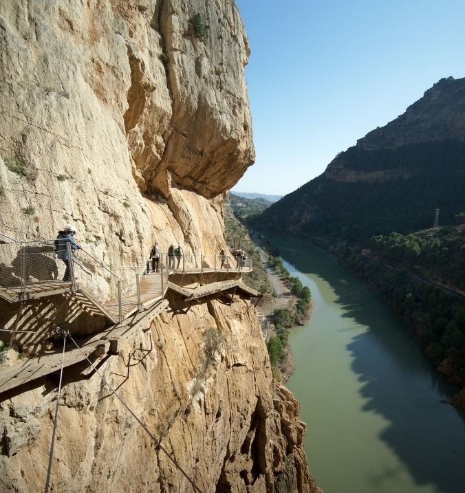 Adventurers walking along a cliffside path near La Cala overlooking a river canyon
